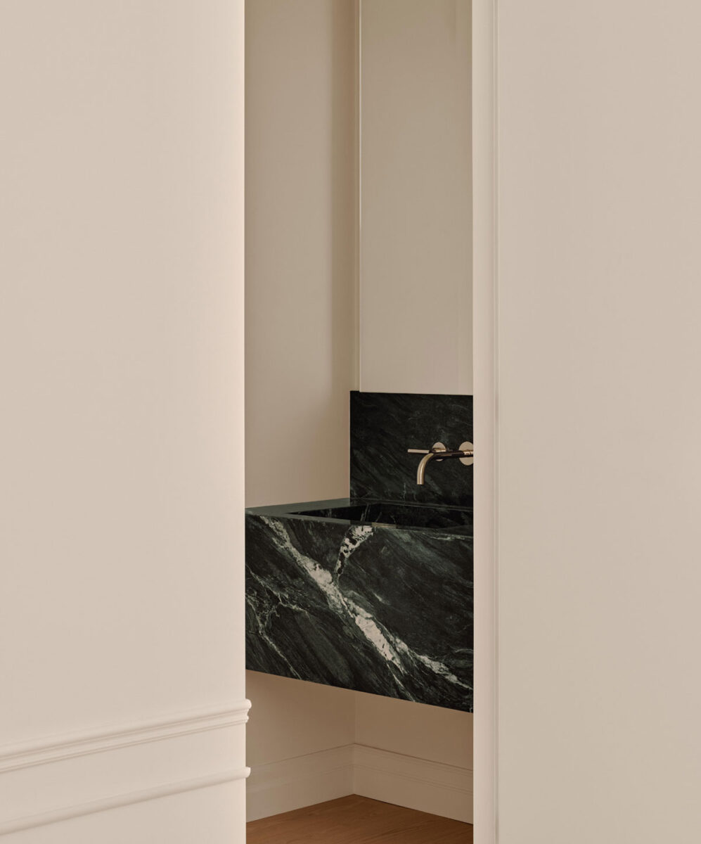Small powder room beneath staircase with sculptural marble sink and concealed door