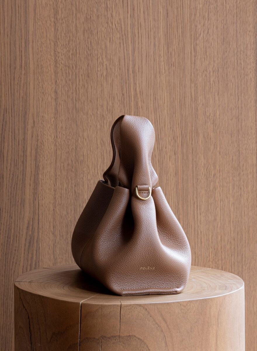 A sculptural Polène handbag on a rounded wooden pedestal.