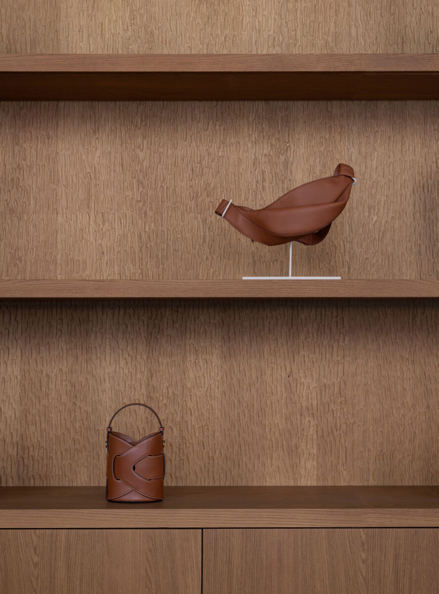 Polène brown leather purses displayed on oak shelves.