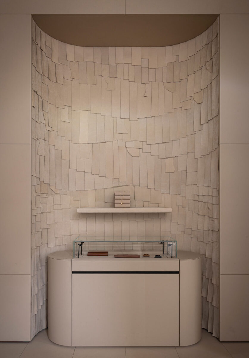 Nude display counter against a wall of layered leather shingles.