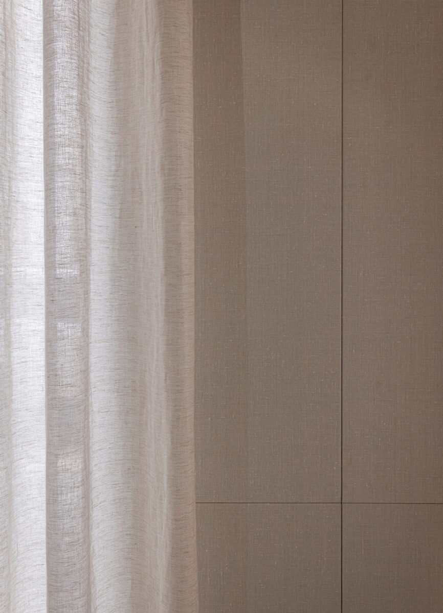 Sheer curtain beside a pale textured wall.
