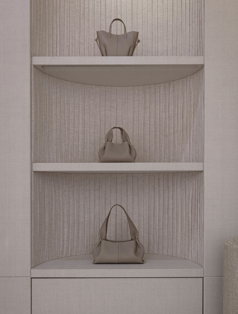 Three sculptural leather handbags displayed on shelves backed by pleated fabric.