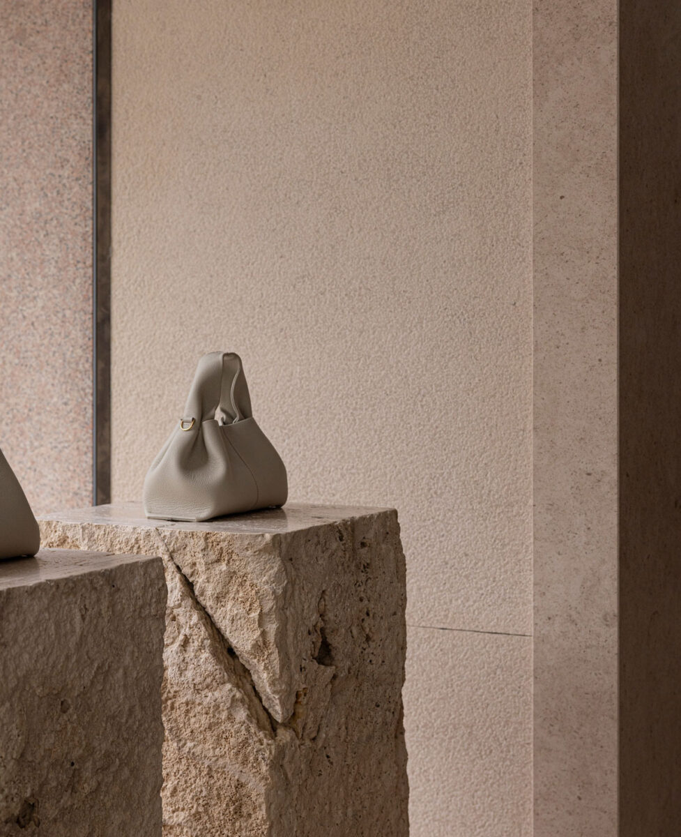 A sculptural handbag on a raw stone pedestal.