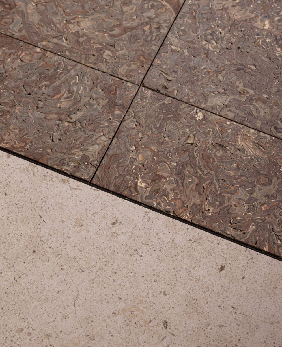 Compressed leather floor tiles beside pale stone flooring.