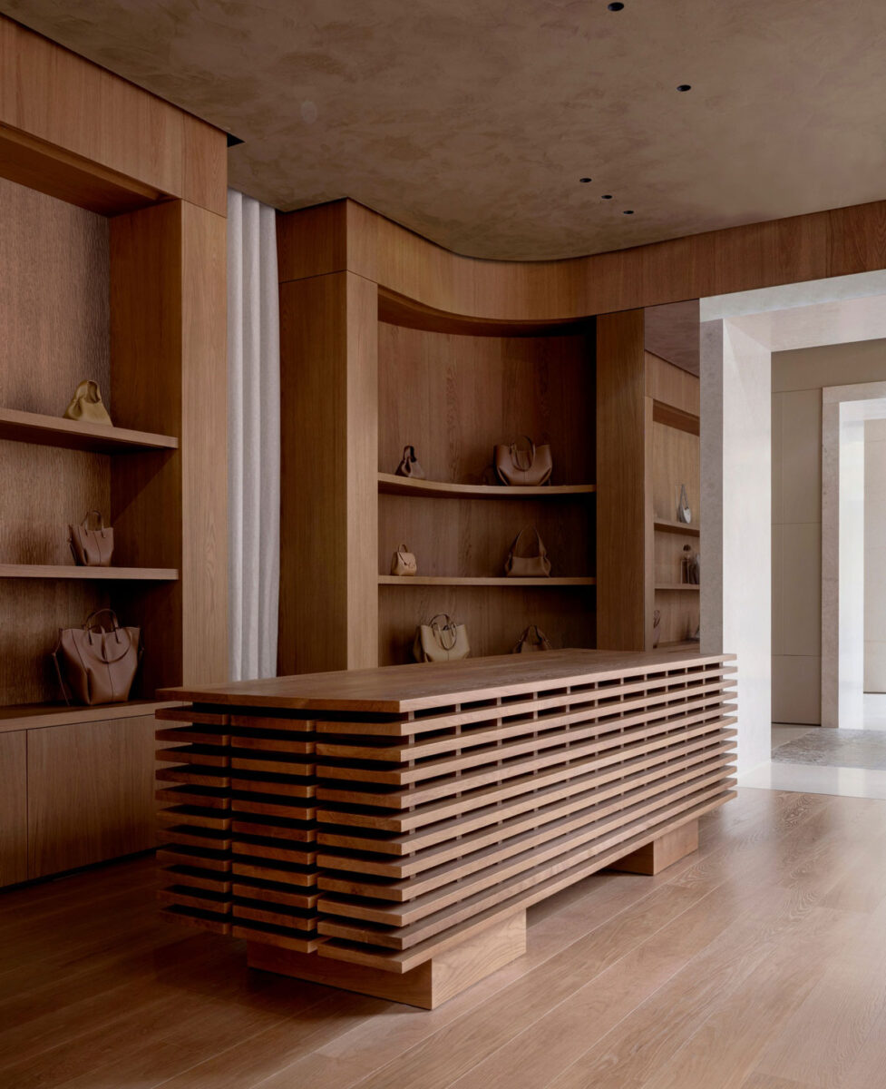 Handbags displayed among custom curved oak shelving and a slatted wooden table.