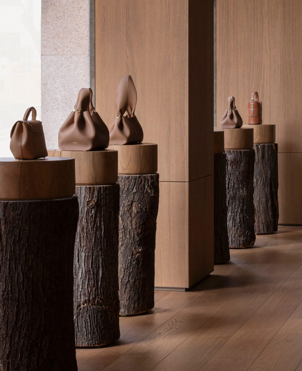 Leather handbags displayed on bark-covered log pedestals.