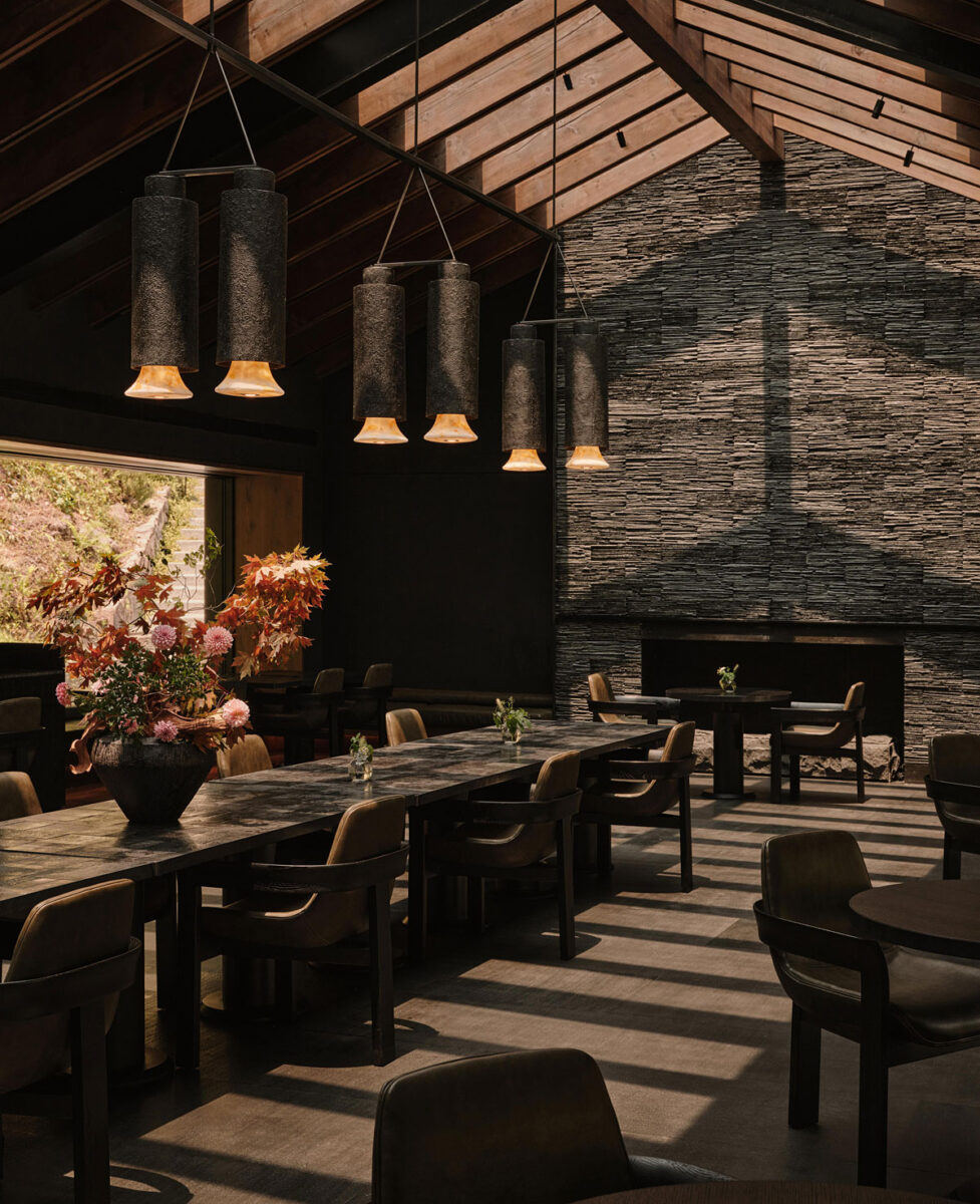 Moody restaurant with wood ceiling beams, a stone fireplace wall, and sculptural pendant lighting