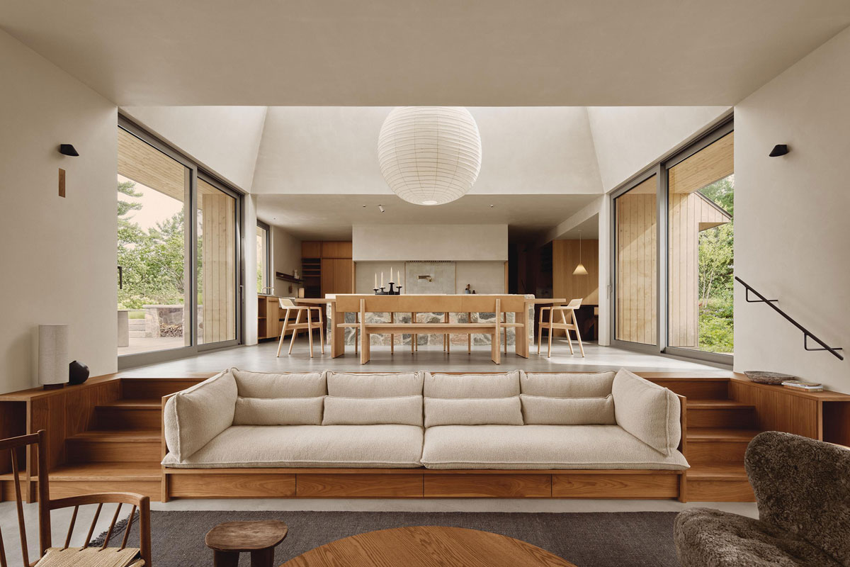 Pine Island Cottage living room with a custom walnut sofa, stepped floors, and tall windows framing island greenery.
