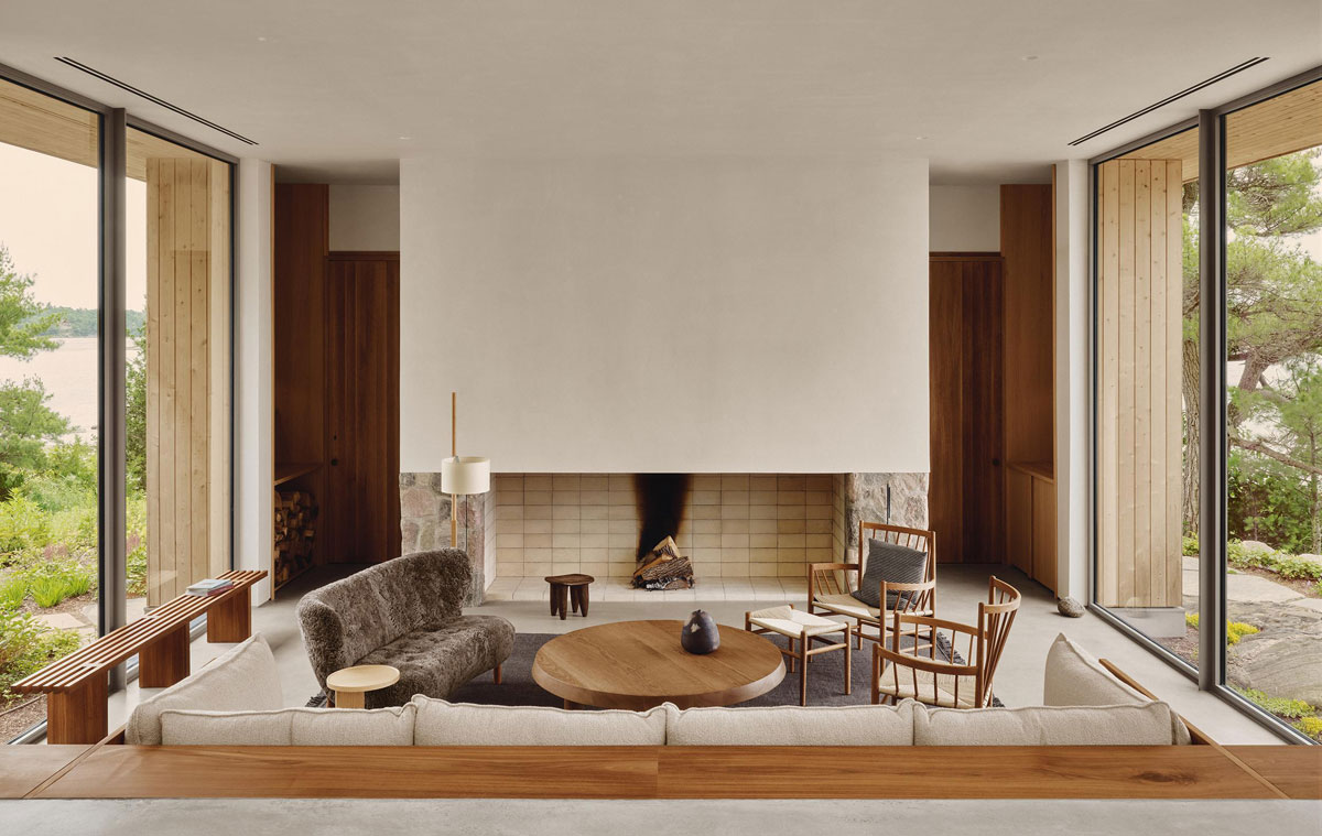 Sunken living room at Pine Island Cottage with a fieldstone fireplace, custom sofa, and windows overlooking rocky terrain.