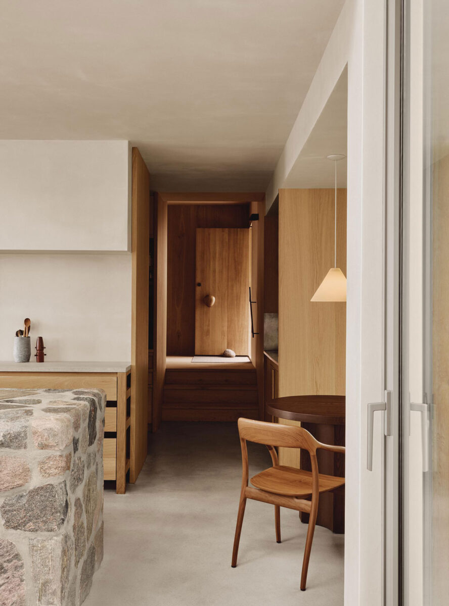 View past the fieldstone kitchen island toward steps and an oak-paneled walls.