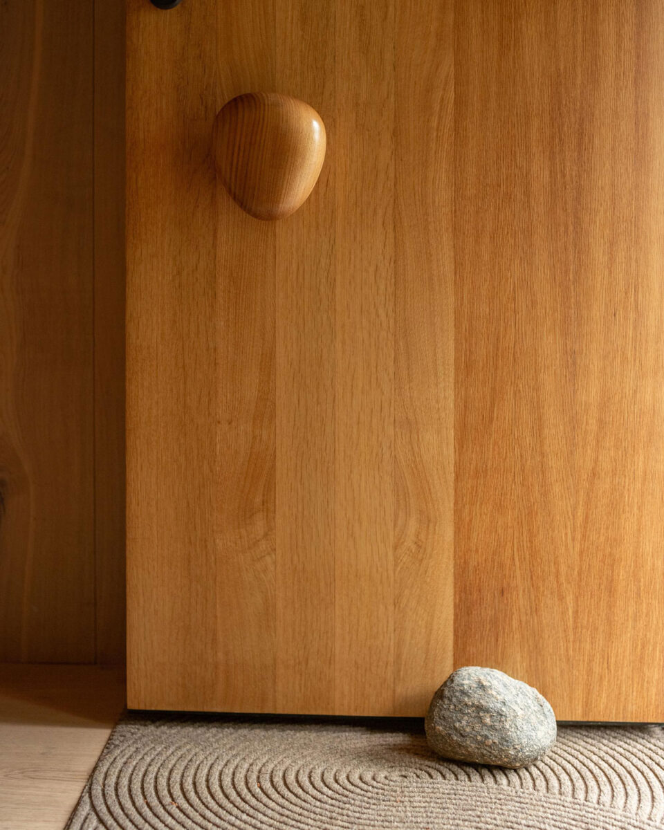 Pebble-shaped oak door handle above a woven rug and rounded stone doorstop.