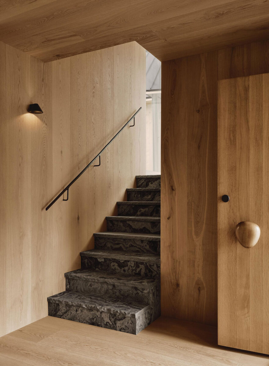 Stone staircase with a wrought-iron handrail, oak wall paneling, and a small wall sconce.