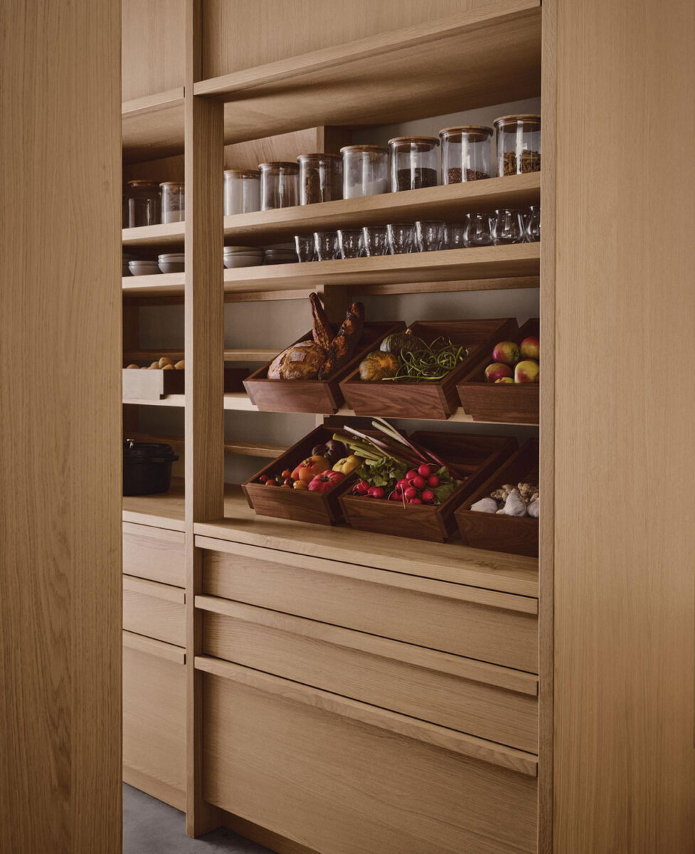 Custom oak pantry with open shelves, glass storage jars, and removable wooden trays filled with fresh produce.