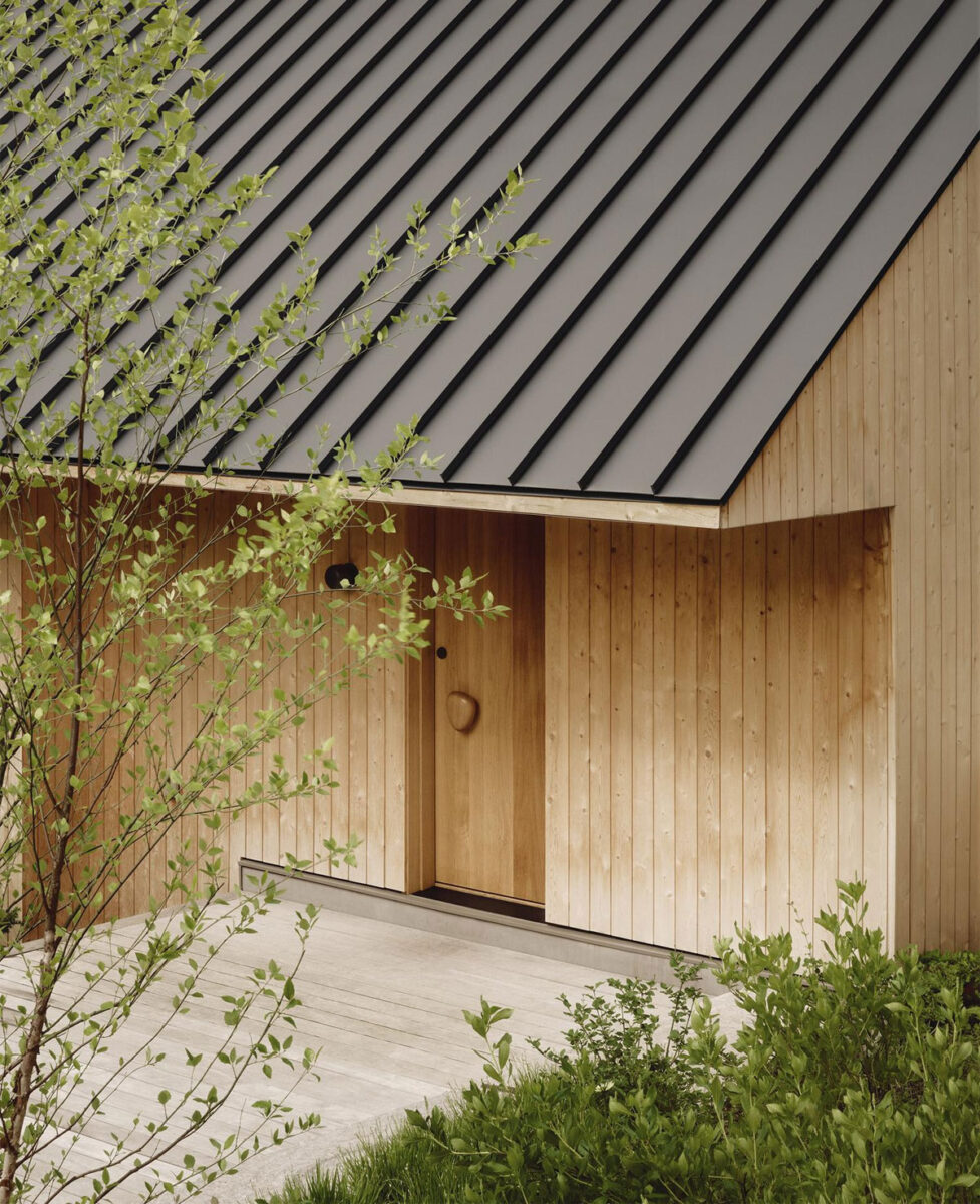 Pine Island Cottage exterior with vertical wood cladding, a dark standing-seam roof, and surrounding greenery.