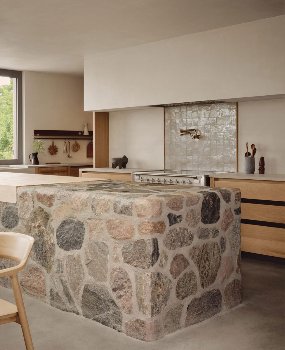 Fieldstone-clad kitchen island with a pale stone countertop, oak cabinetry, and a tiled backsplash.