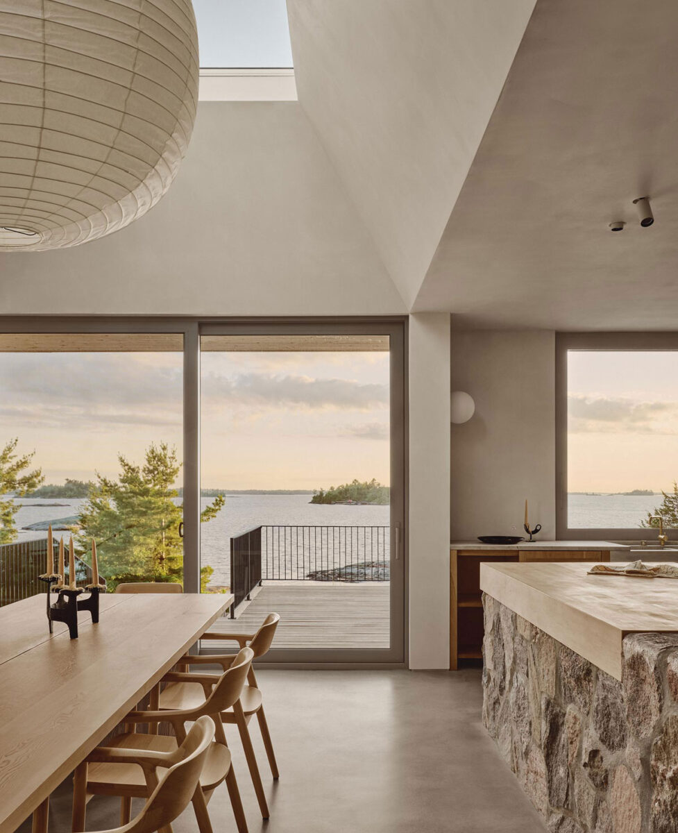 Timber dining table beside a fieldstone kitchen island, with glass doors opening toward Georgian Bay.